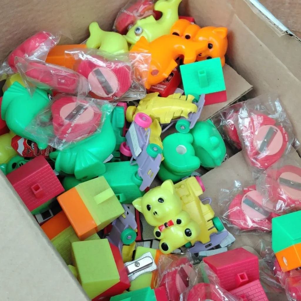 Caja llena de sacapuntas y juguetes de plástico de colores variados. by Remates Narvaja