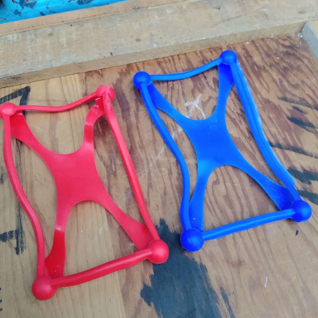 Dos ejercitadores de mano de silicona flexibles, uno rojo y uno azul, para fortalecimiento de agarre. by Remates Narvaja