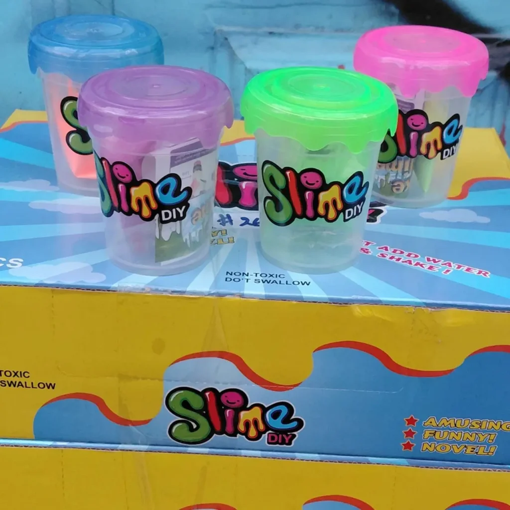 Cuatro vasos de Slime DIY con tapas de colores sobre una caja de producto. by Remates Narvaja