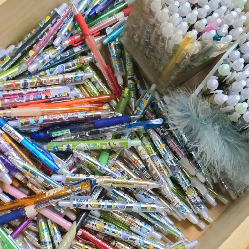 Un gran montón de bolígrafos y lápices de colores con diseños de dibujos animados, junto a pequeñas botellas de suministros de arte y plumas by Remates Narvaja
