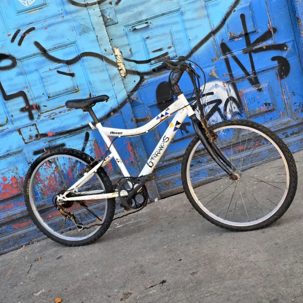 Bicicleta blanca urbana frente a una puerta azul con graffiti. by Remates Narvaja