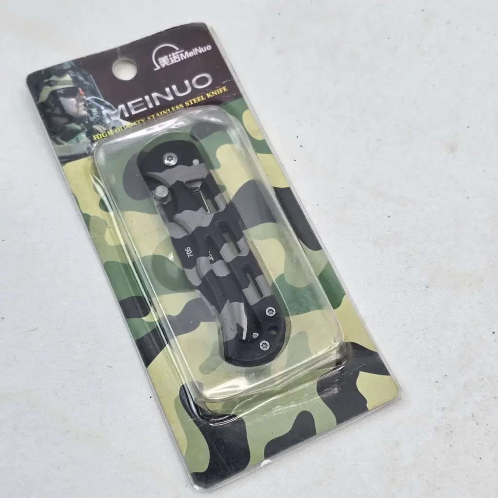 Cuchillo plegable MeiNuo de acero inoxidable, negro y gris camuflado, en blíster con fondo de camuflaje. by Remates Narvaja