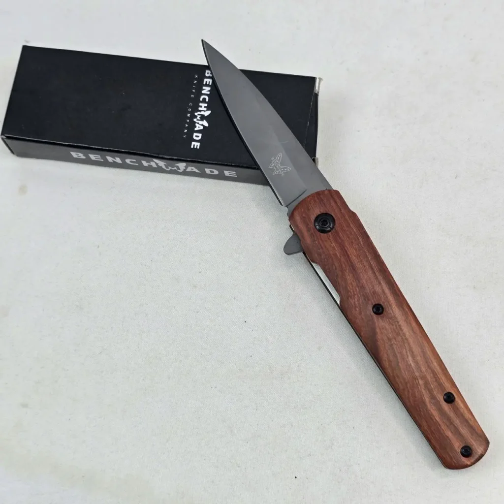 Navaja Benchmade con mango de madera y hoja oscura, junto a su caja. by Remates Narvaja