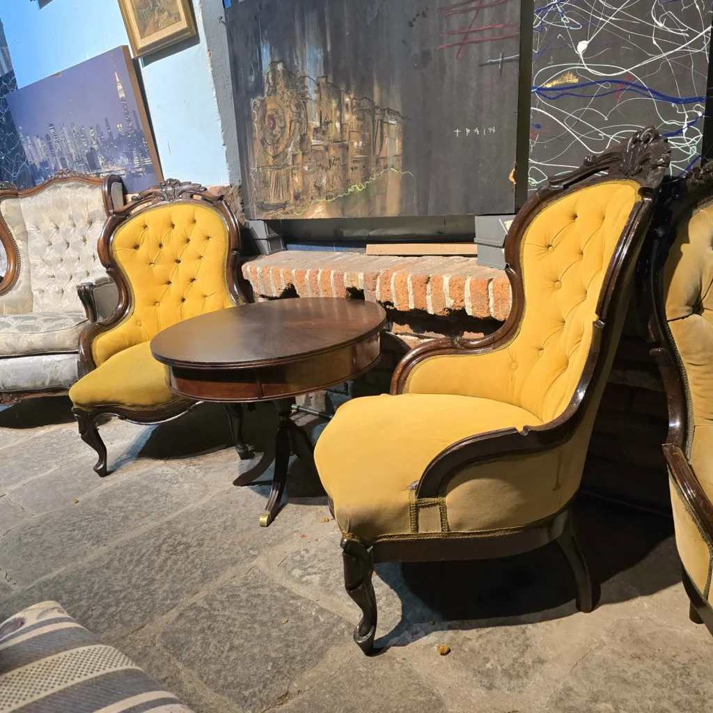 Dos sillones antiguos de terciopelo amarillo y una mesa de madera oscura con cuadros de tren y ciudad de fondo." by Remates Narvaja
