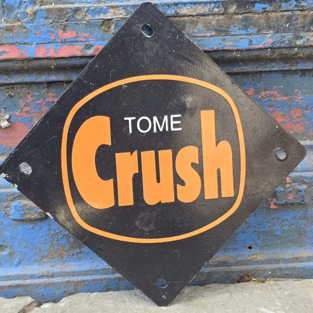 Letrero vintage negro de "TOME Crush" con letras naranjas sobre una pared desgastada. by Remates Narvaja