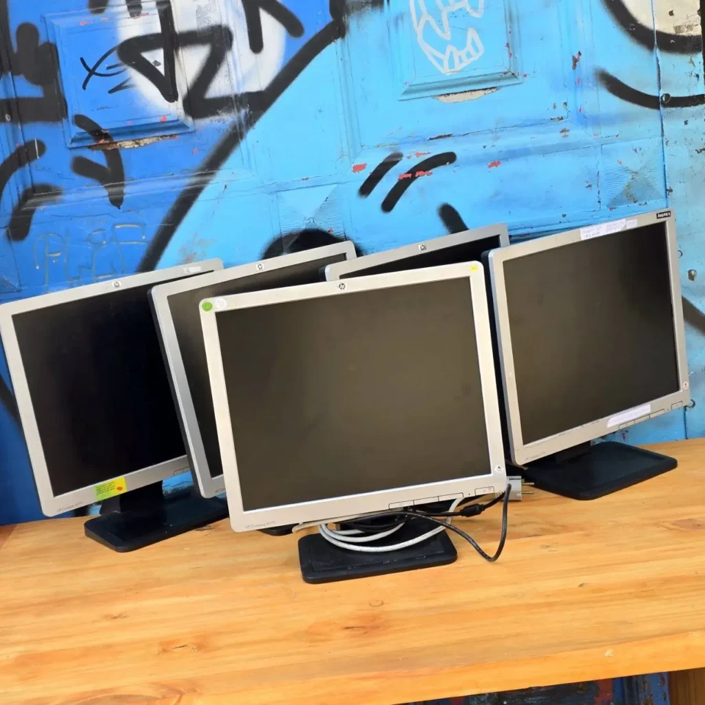 Varios monitores HP Compaq usados sobre una mesa de madera, con fondo de graffiti azul. by Remates Narvaja