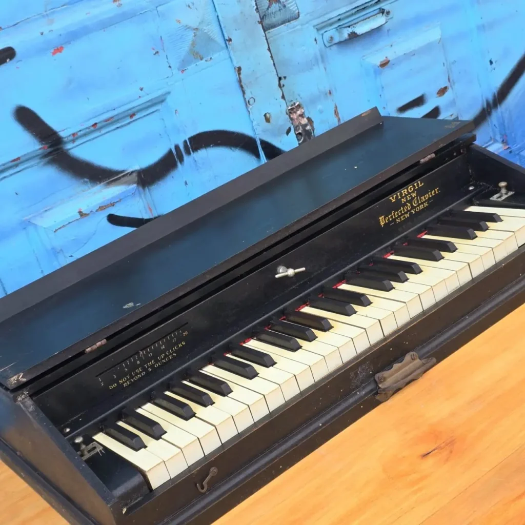 Virgil Perfected Clavier, instrumento musical antiguo de práctica con teclado negro y blanco, sobre suelo de madera y fondo azul. by Remates Narvaja