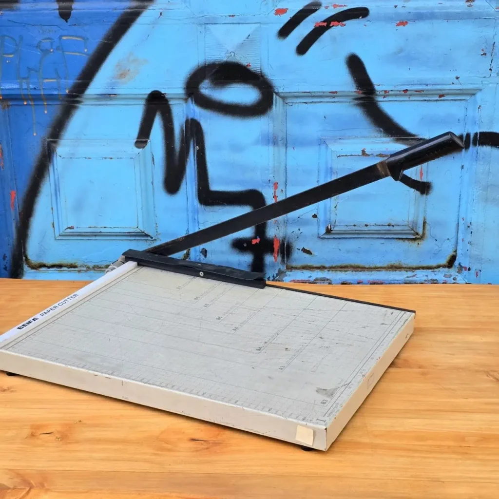 Cortadora de papel BEIFA gris sobre mesa de madera, fondo azul con graffiti. by Remates Narvaja