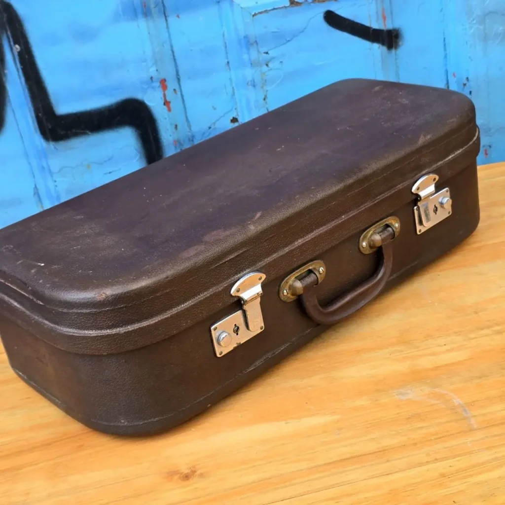 Estuche vintage marrón oscuro con cerraduras y asa sobre madera, fondo azul. by Remates Narvaja