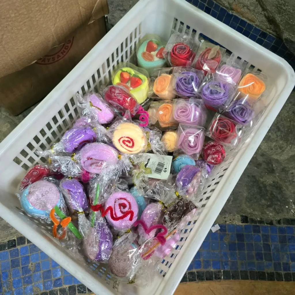 Cesta blanca con toallas pequeñas de colores variados en formas de rosas y pasteles, envueltas individualmente. by Remates Narvaja
