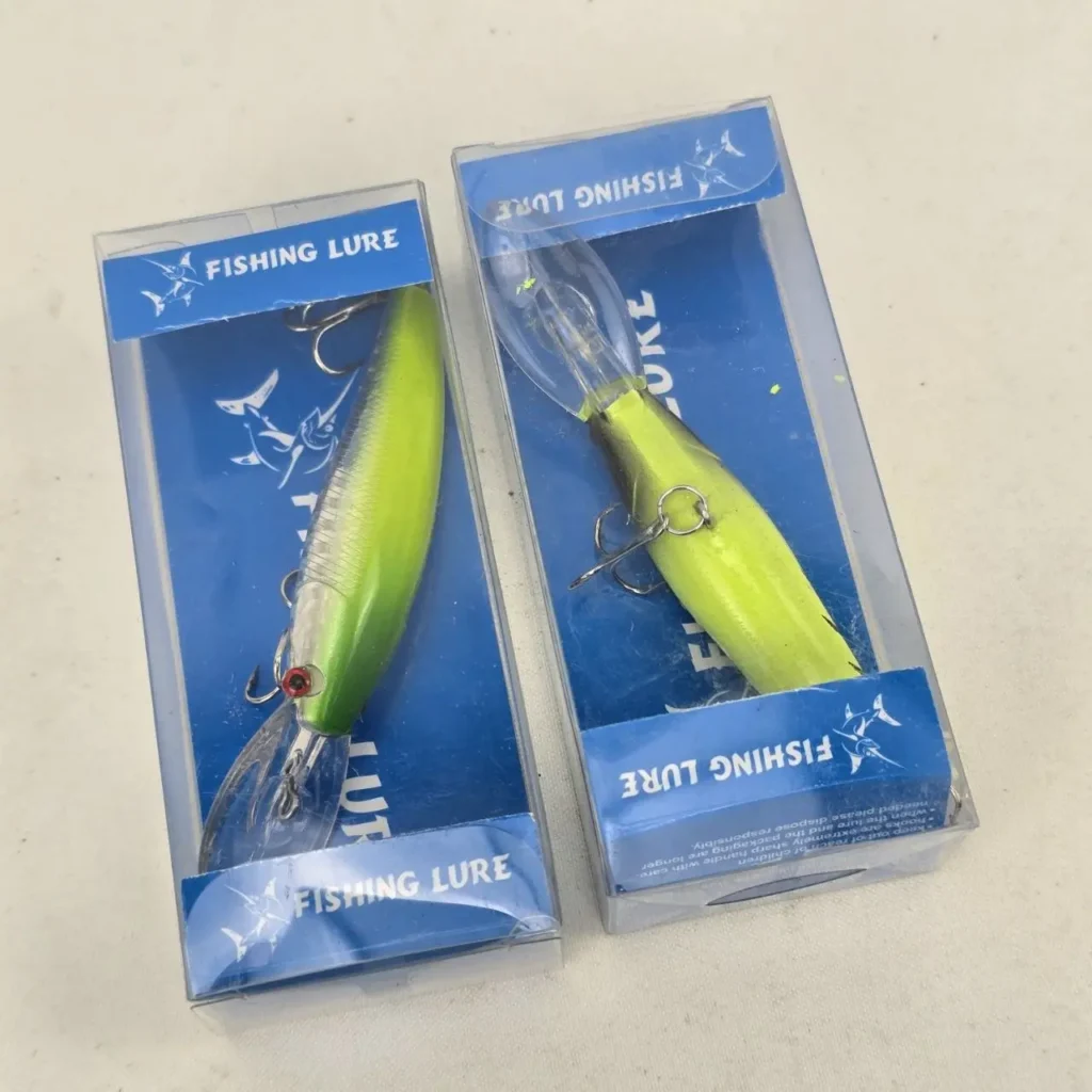Dos señuelos de pesca artificiales, uno verde y otro amarillo, en sus empaques con la etiqueta "FISHING LURE". by Remates Narvaja