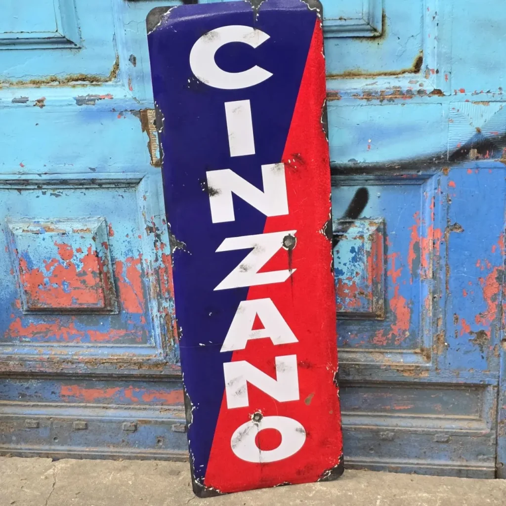 Letrero vintage de Cinzano azul y rojo contra una puerta azul descascarada." by Remates Narvaja