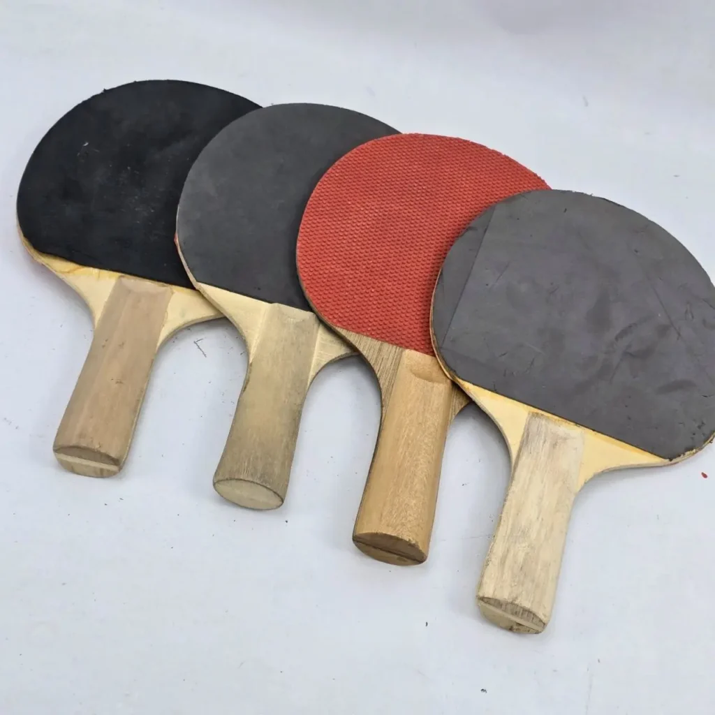 Cuatro palas de ping pong con mangos de madera y gomas negras y una roja. by Remates Narvaja