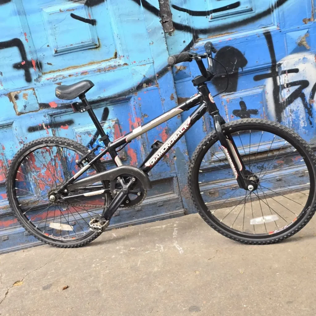 Bicicleta Diamondback negra contra puerta azul con grafitis. by Remates Narvaja