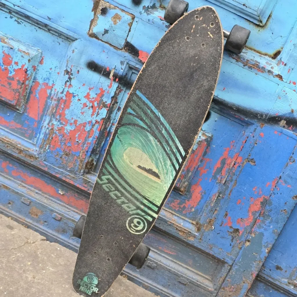 Sector 9 longboard con gráfico de ola sobre puerta azul desgastada. by Remates Narvaja