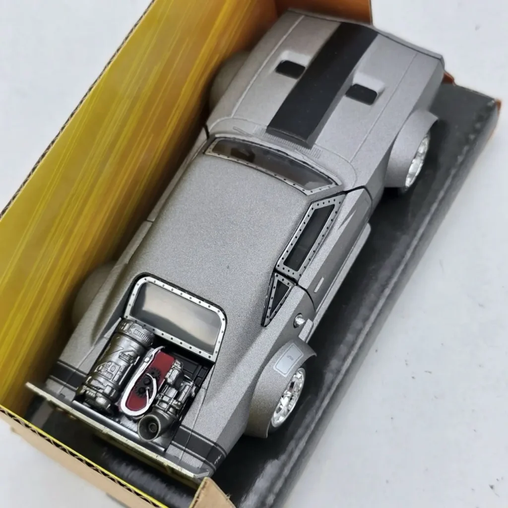 Maqueta de coche plateado con franjas negras, motor expuesto y diseño futurista en su caja. by Remates Narvaja